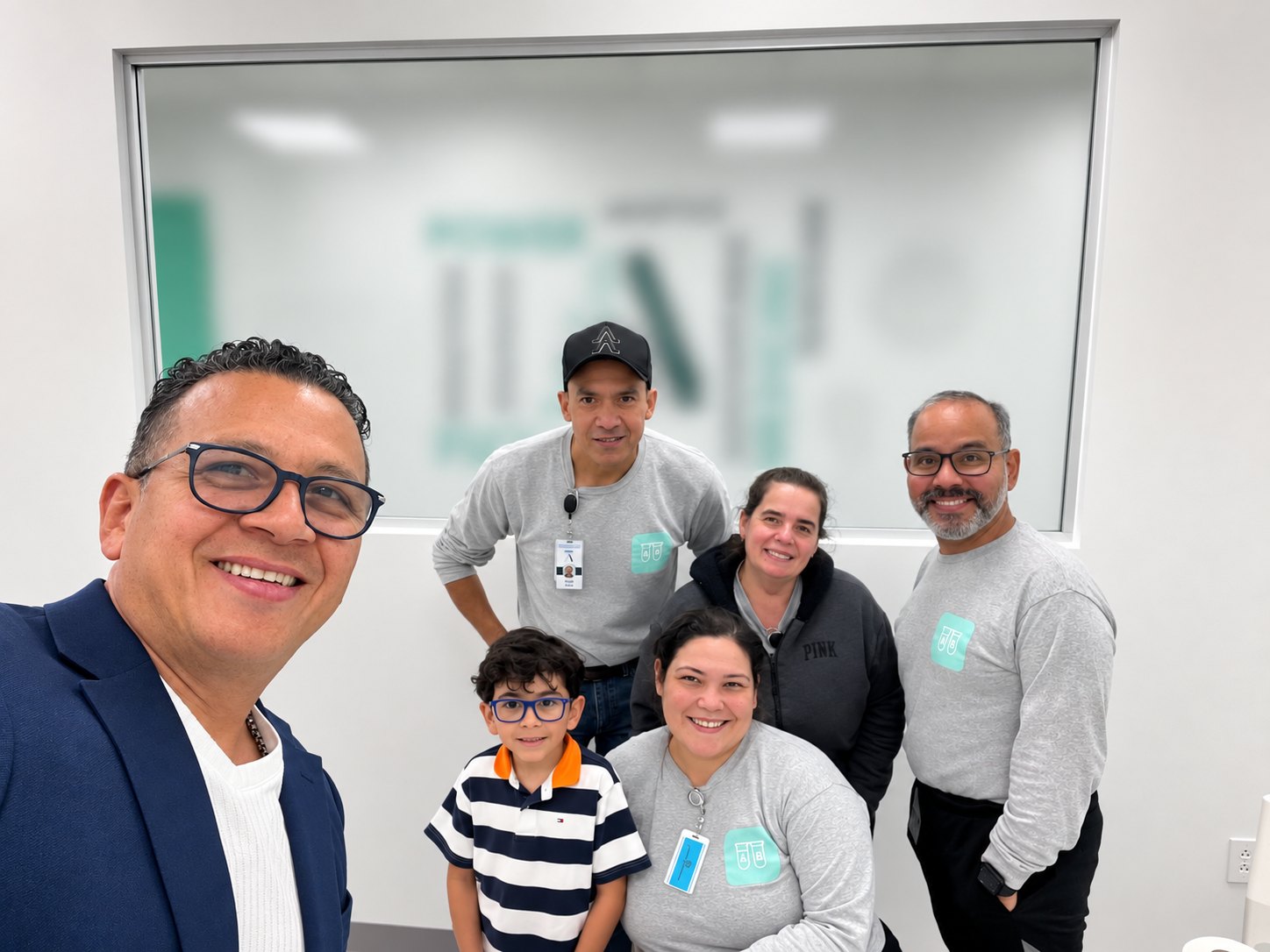A group from the AB CleanRoom Services team inside a client facility, wearing grey company shirts carrying the AB test-tube mark, gathered in front of an interior window.